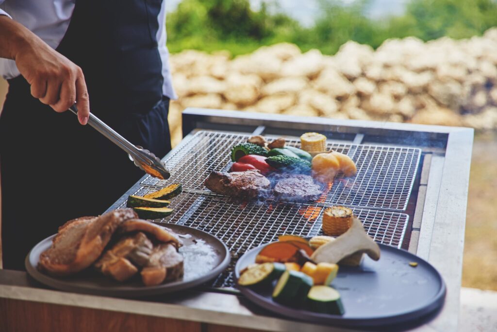 スタッフが焼き上げるグリル料理とカラフルな夏野菜(屋外バーベキュー)
